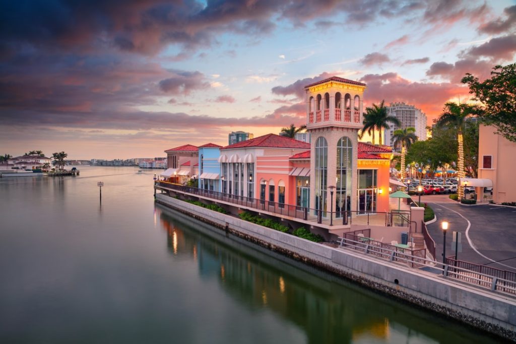 Mediterraans aandoend gebouw met een vierkante toren aan een kade, gefotografeerd tijdens een kleurrijke zonsondergang