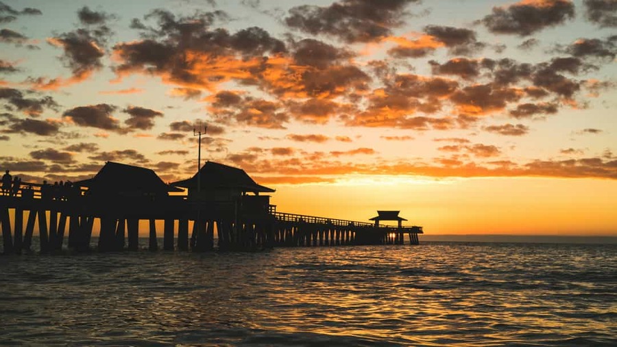 Silhouet van de houten pier van Naples in Florida met mensen die genieten van een kleurrijke zonsondergang boven zee