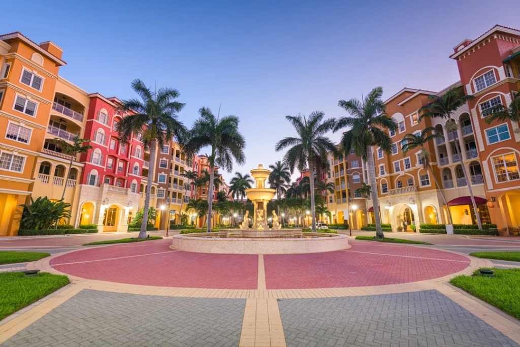 Rond plein met een verlichte fontein omringd door palmbomen en oranje en rode gebouwen in mediterrane stijl in Naples in Florida
