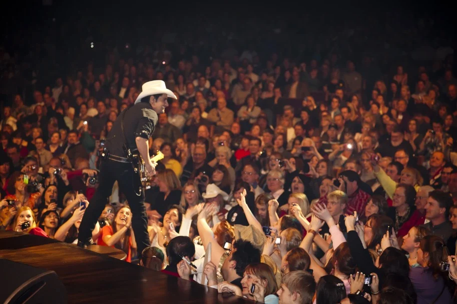 Countryzanger met witte hoed en gitaar op het podium van de Grand Ole Opry terwijl een grote menigte fans juicht
