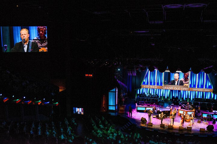 Zicht vanuit de zaal op een band die optreedt op het verlichte podium van de Grand Ole Opry