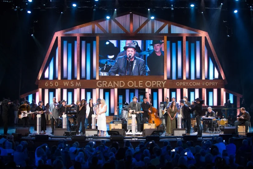 Een groep muzikanten staat op het verlichte podium van de Grand Ole Opry in Nashville, met publiek op de voorgrond