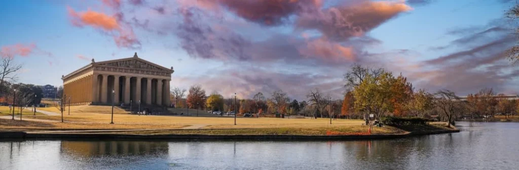 Volledige replica van het Griekse Parthenon met zuilen weerspiegeld in het water in Nashville onder een kleurrijke avondlucht