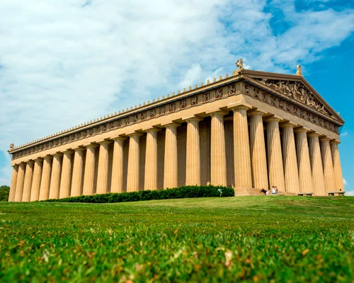 De volledige lengte van de Parthenon replica met rijen zuilen gezien vanaf het grasveld ervoor onder een wolkenlucht