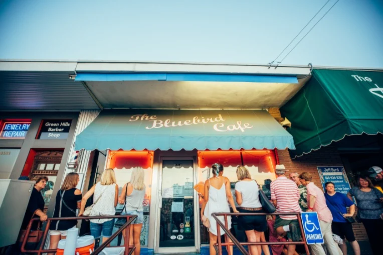 Een groep mensen staat buiten in de rij voor het beroemde Bluebird Cafe in Nashville onder een blauwe luifel