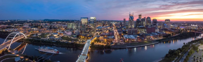 Luchtfoto van de skyline van Nashville met verlichte wolkenkrabbers langs de rivier tijdens een kleurrijke zonsondergang