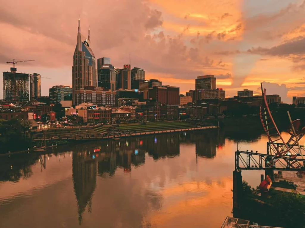 De skyline van Nashville weerspiegelt in de rivier terwijl een voetgangersbrug over het water leidt bij een felle zonsondergang