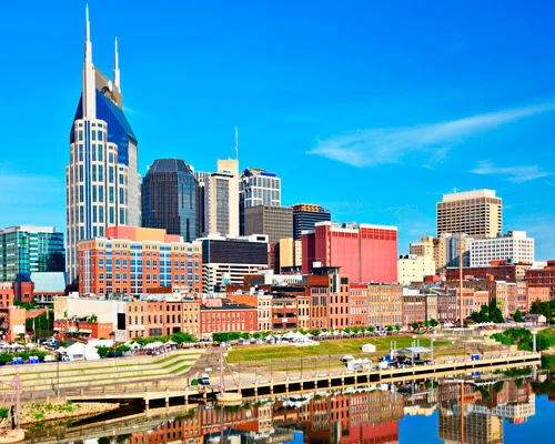 Zonnige skyline van Nashville met de kenmerkende torenspitsen van het AT&T gebouw en de rivier die de wolkenkrabbers weerspiegelt