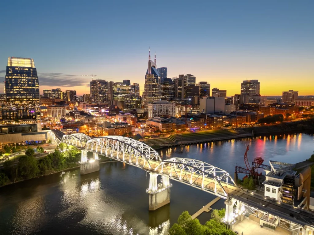 De verlichte skyline van Nashville met een boogbrug over de rivier op de voorgrond in de vallende avond