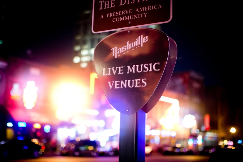 Een straatbord met de tekst Live Music Venues staat voor felverlichte gevels van clubs in Nashville in de avond
