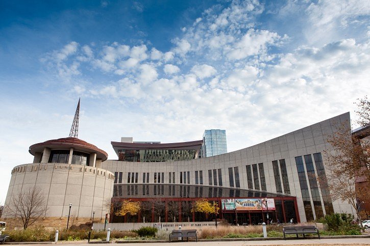Golvend gebouw van natuursteen met een ronde toren van de Country Music Hall of Fame in Nashville tegen een blauwe lucht met wolken