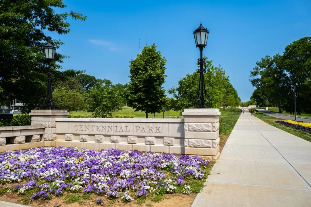 Stenen bord met de tekst Centennial Park bij een pad met straatlantaarns en een perk vol paarse bloemen in Nashville