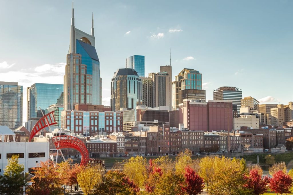 Skyline van Nashville met de kenmerkende torenspitsen van het AT&T gebouw en een rood reuzenrad, met bomen in herfstkleuren op de voorgrond