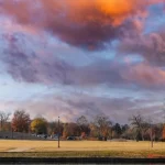 De replica van het Griekse Parthenon staat tussen bomen in een park terwijl de wolken oranje kleuren bij zonsondergang
