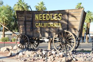 Oude houten huifkar met de tekst Needles California erop, opgesteld tussen palmbomen als landmark