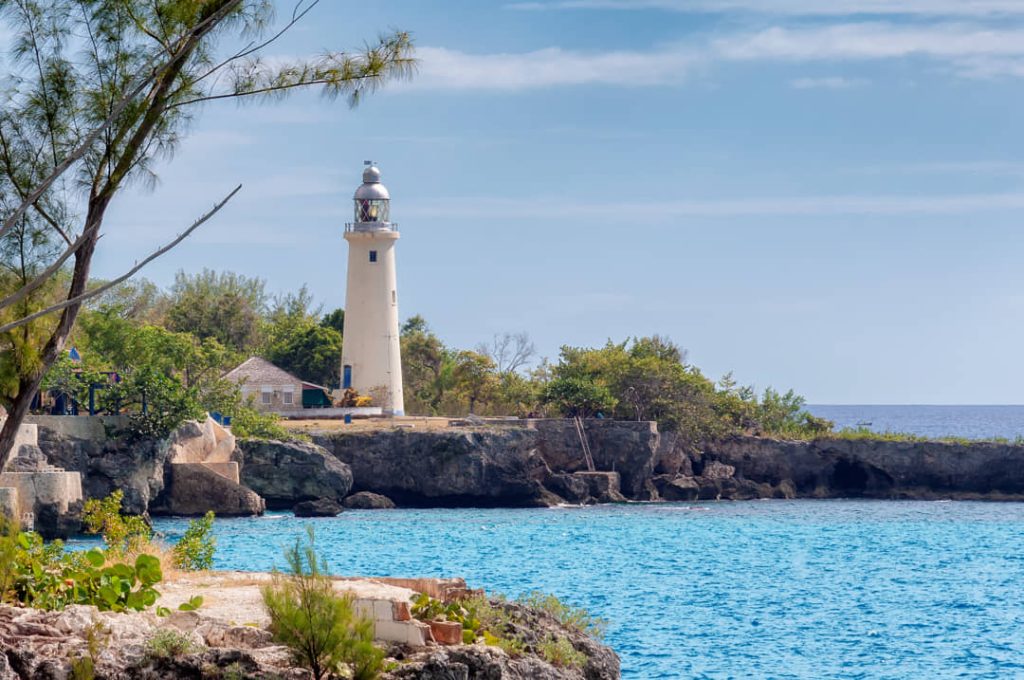 Witte vuurtoren Negril Lighthouse op een rotsachtige landtong met helder blauwe zee op de achtergrond