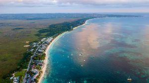 Luchtfoto van het lange witte strand van Negril met turquoise water, aangemeerde bootjes en groene kustvegetatie