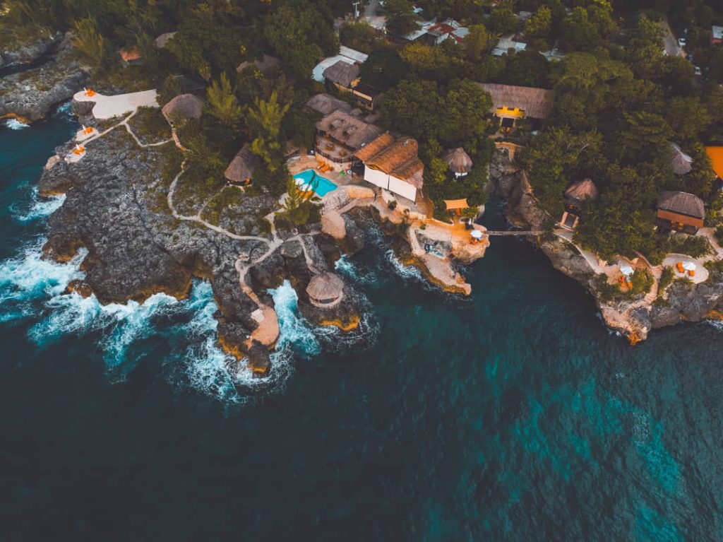 Luchtfoto van een klifresort met strohutten en zwembad op de rotsen van West End in Negril, omringd door helder water