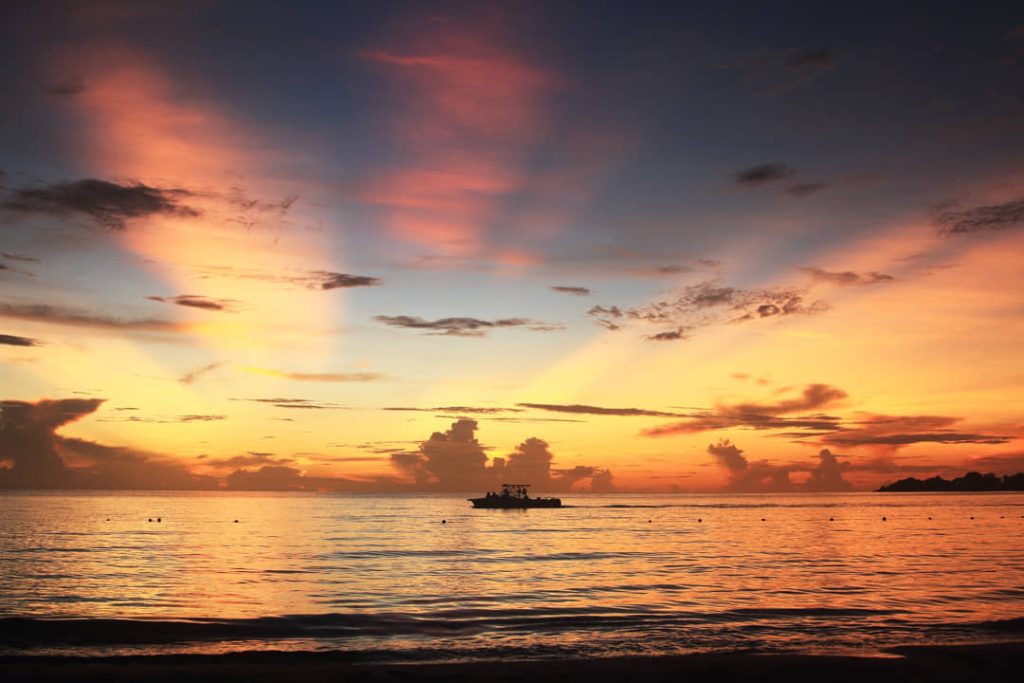 Dramatische zonsondergang boven zee met lichtstralen door de wolken en een silhouet van een vissersboot op het water