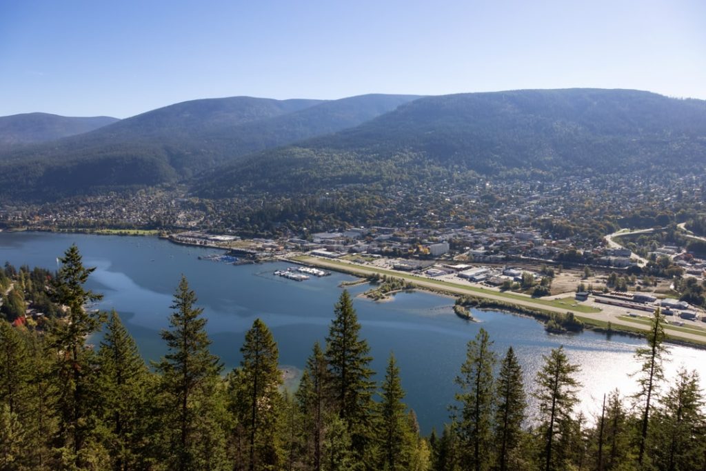 Luchtfoto van de stad Nelson aan een blauw meer omringd door beboste bergen onder een zonnige hemel