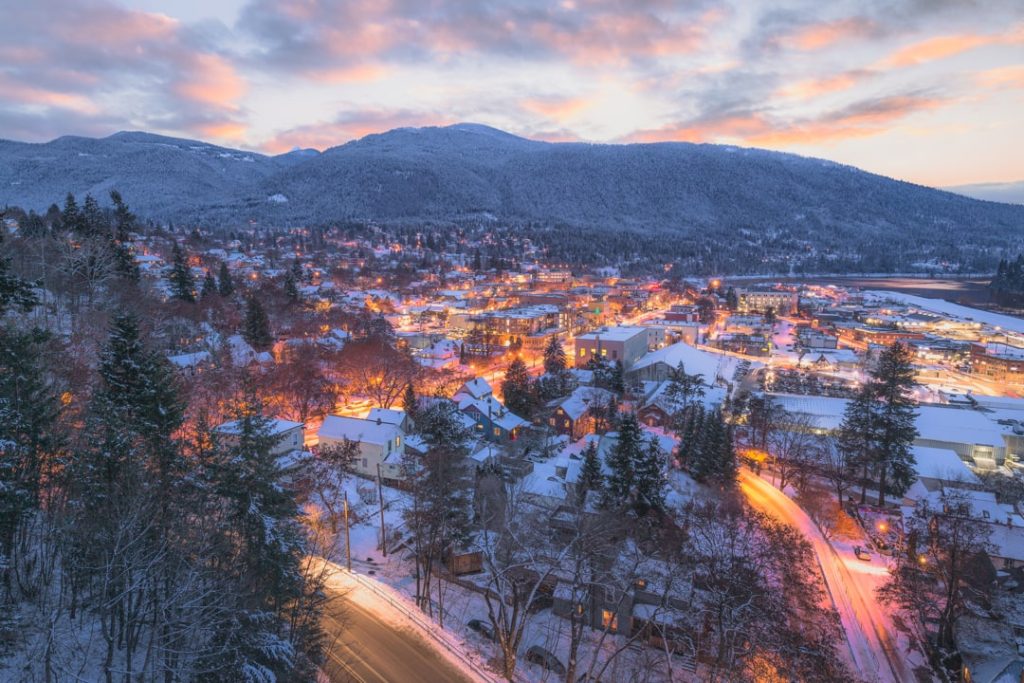 Luchtfoto van een besneeuwde stad met verlichte huizen tegen een berg tijdens een roze gekleurde winterse schemering