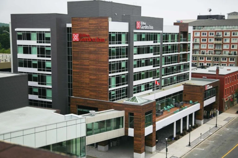 Een modern hotelgebouw met houten en glazen gevel torent boven omliggende gebouwen uit in een stadscentrum in New Brunswick