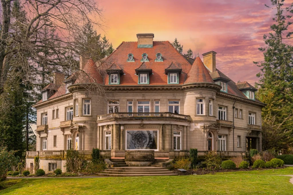Groot stenen herenhuis met torentjes en een rood dak tegen een roze en oranje avondlucht in New England