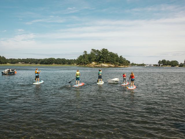 Vijf mensen op suppboards peddelen in een rij over kalm water langs een klein bebost eilandje in New Hampshire