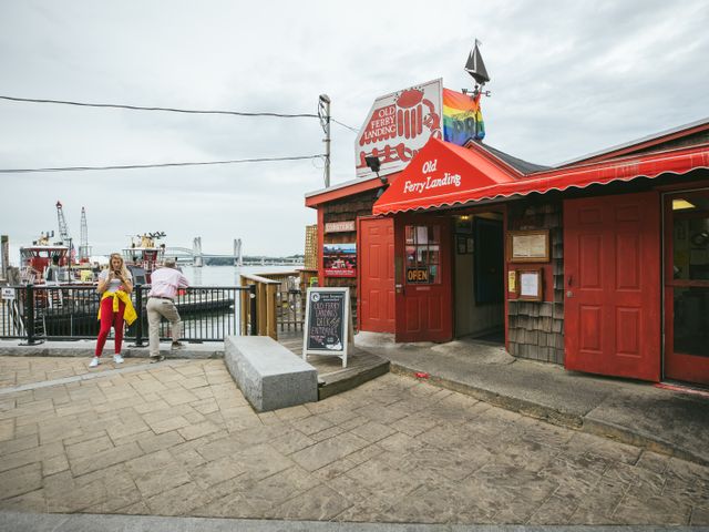 Rood houten restaurant met de naam Old Ferry Landing en een regenboogvlag op het dak, met een brug over het water op de achtergrond in New Hampshire