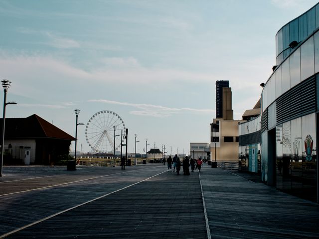 Houten boardwalk langs de kust van New Jersey met in de verte een reuzenrad, wandelaars en gebouwen in de avondzon