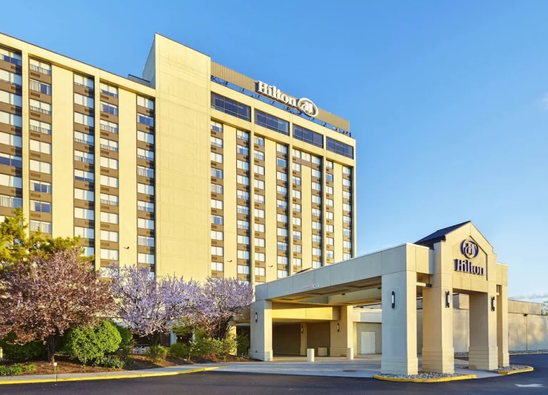 Hoog hotelgebouw van Hilton met een overdekte ingang en roze bloesembomen ervoor onder een strakblauwe hemel in New Jersey