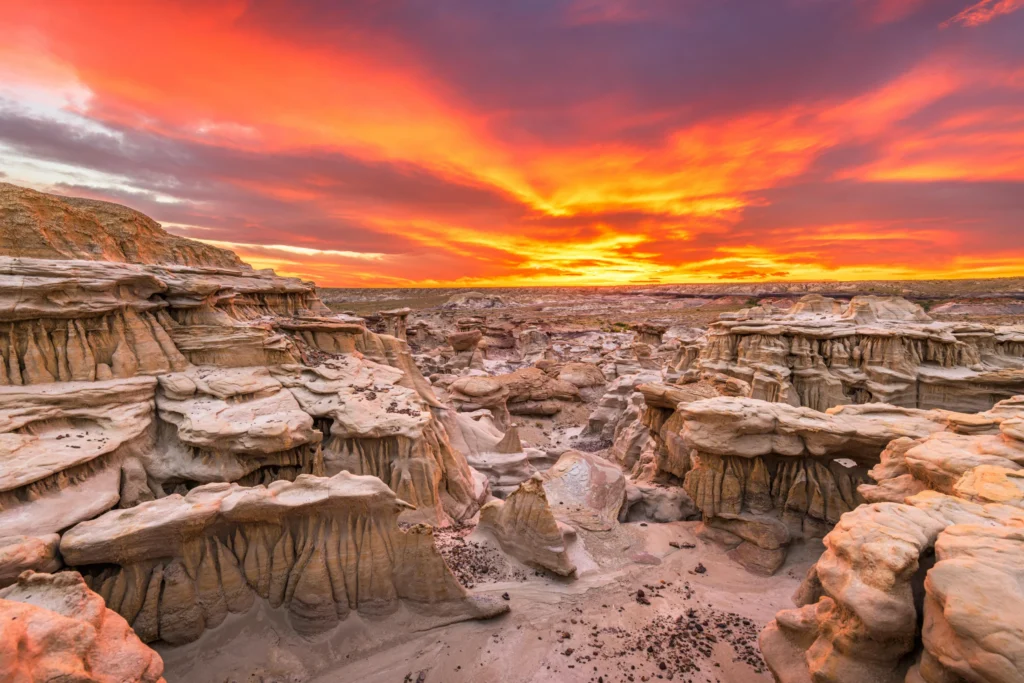 Grillige rotsformaties in een droog landschap onder een vurige oranje en paarse zonsondergang in New Mexico