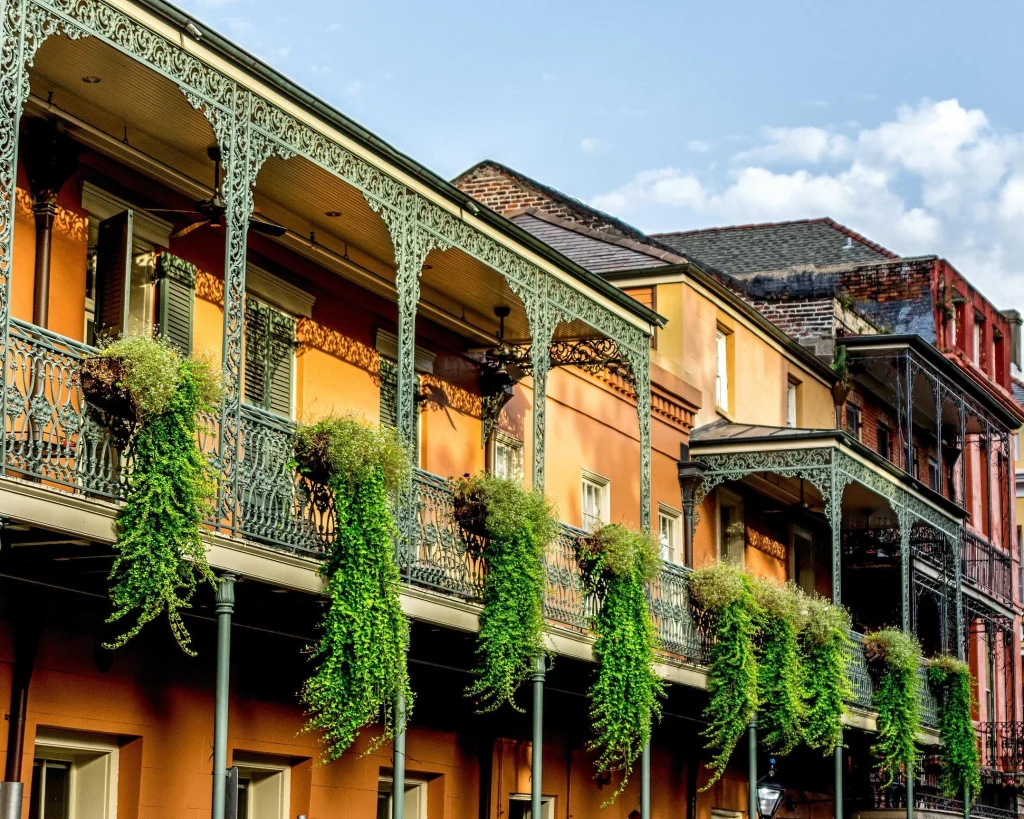 Rij smeedijzeren balkons met weelderige hangplanten aan oranje en rode gevels in de French Quarter van New Orleans