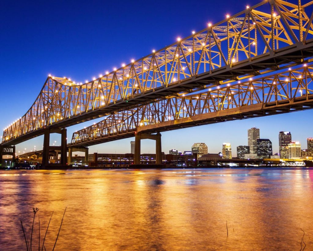 Verlichte stalen brug over de Mississippi rivier met de skyline van New Orleans op de achtergrond bij zonsondergang