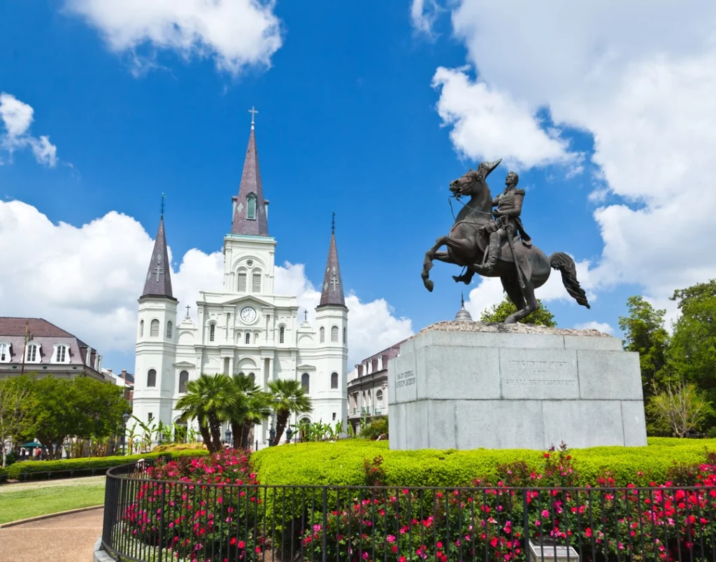Wit kathedraalgebouw met spitse torens en een bronzen ruiterstandbeeld, omgeven door bloemen en groen op Jackson Square in New Orleans