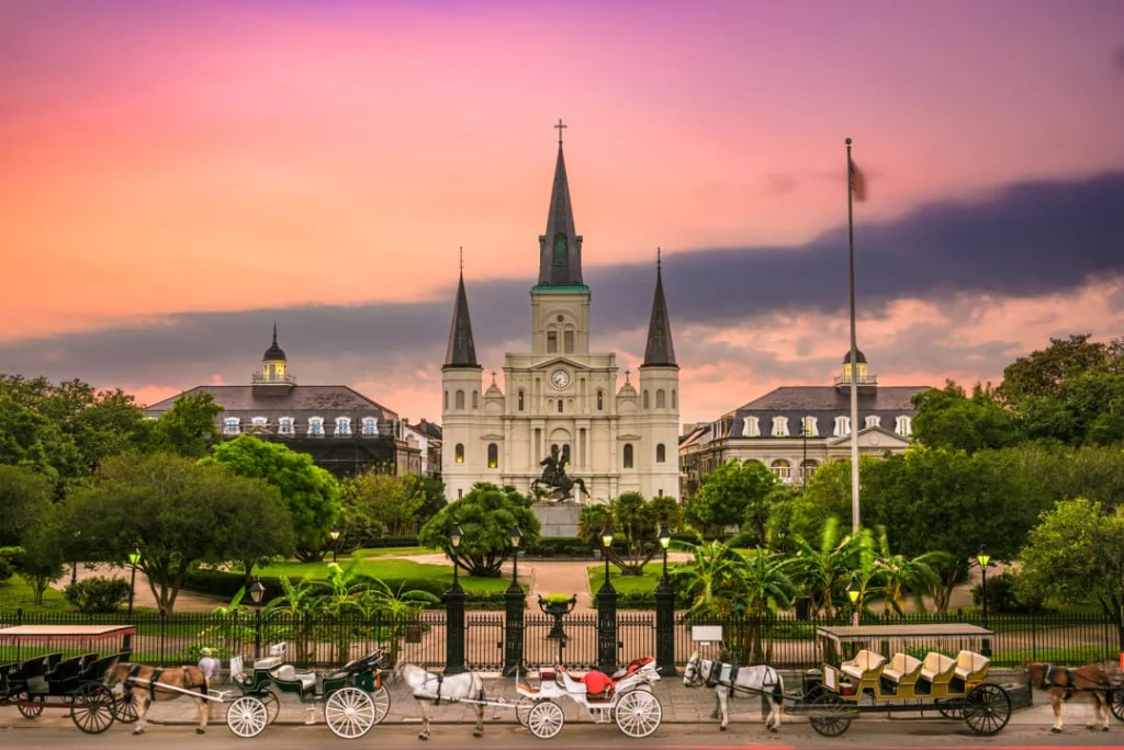 De Sint-Louiskathedraal in New Orleans steekt af tegen een roze avondlucht met koetsen bij het hek van Jackson Square