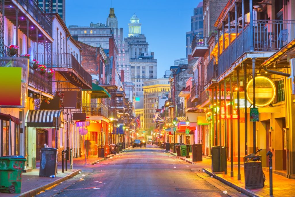 Verlichte straat met balkons vol smeedijzeren hekwerk en neonreclame op Bourbon Street in New Orleans bij het invallen van de avond