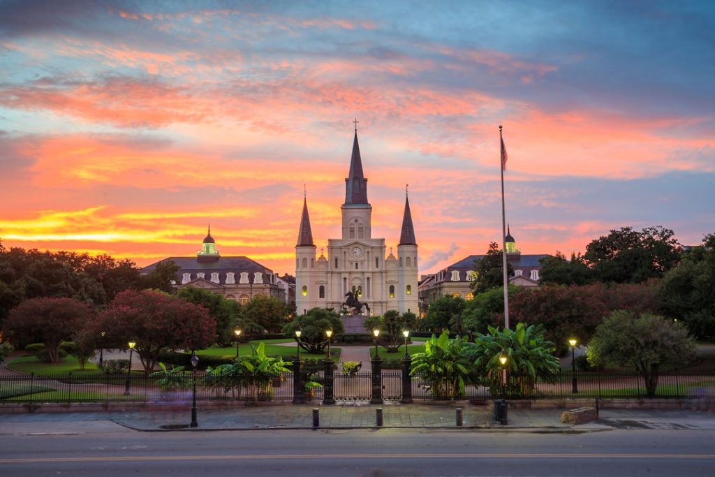 Verlichte kathedraal met drie torenspitsen op Jackson Square in New Orleans tegen een felgekleurde oranje en roze avondlucht