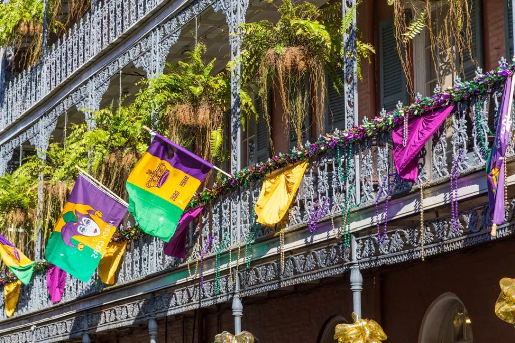 Sierlijk smeedijzeren balkon versierd met paarse, gele en groene Mardi Gras vlaggen en kralenkettingen tussen varens in New Orleans