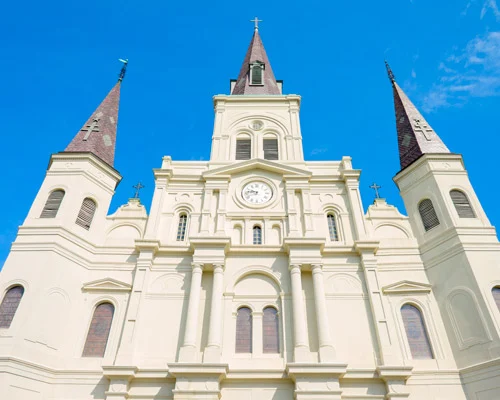 Close-up van de witte gevel en drie spitse torens van de St. Louis Cathedral in New Orleans tegen een heldere blauwe lucht