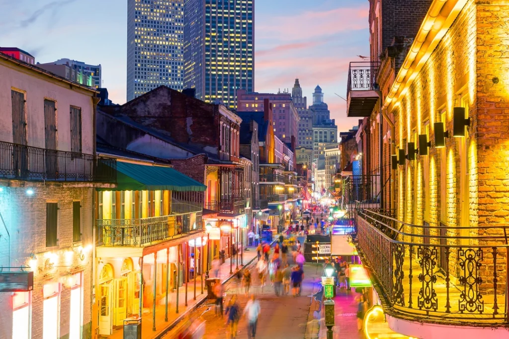 Kleurrijk verlichte balkons en straten van de French Quarter in New Orleans vol wandelaars bij zonsondergang