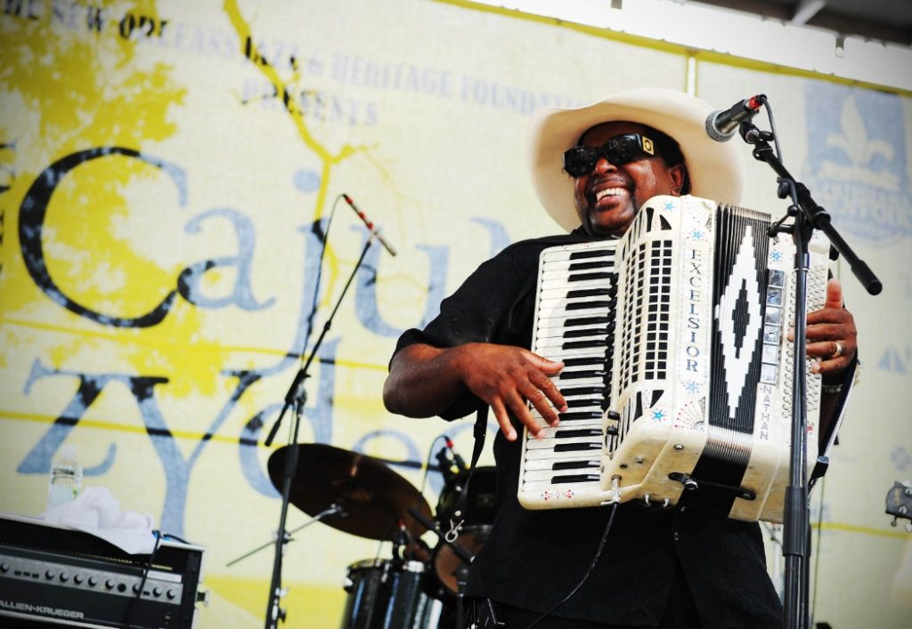 Een lachende muzikant met cowboyhoed en zonnebril speelt accordeon op het podium van het Cajun Zydeco Festival in New Orleans