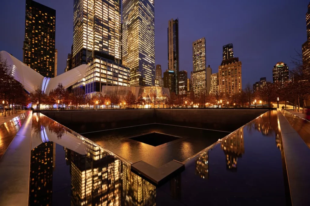 Verlicht 9/11 Memorial in de avond met het reflecterende waterbassin en de skyline van One World Trade Center