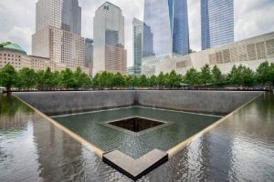 Vierkant waterbekken van het 9/11 Memorial met een waterval naar het middelste gat en wolkenkrabbers van Lower Manhattan op de achtergrond