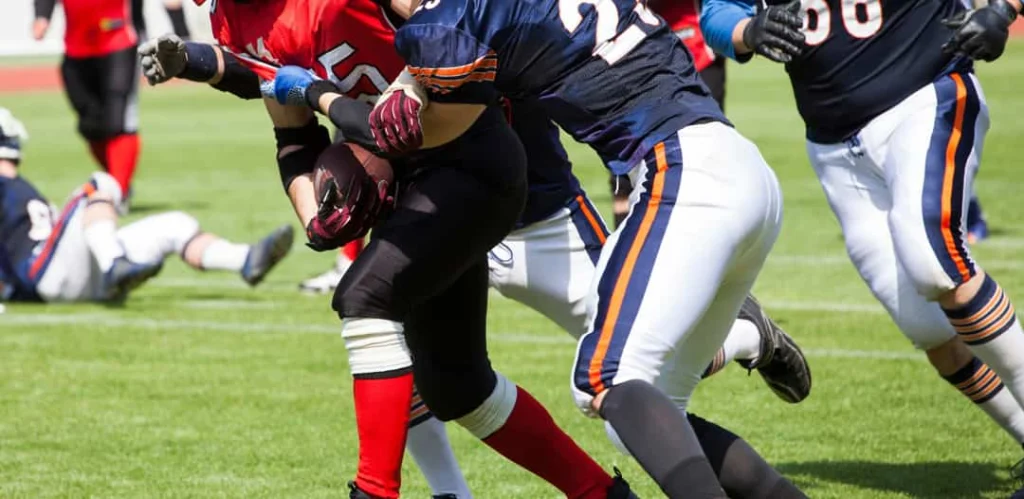 Footballspelers in blauwe en rode tenues botsen op elkaar tijdens een wedstrijd op een grasveld in New York