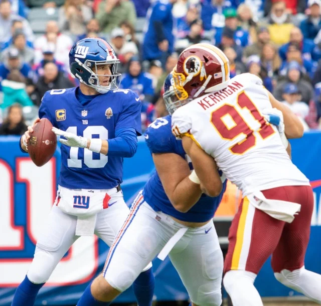 Quarterback van de New York Giants met de bal in de hand tijdens een duel met een tegenstander op het veld