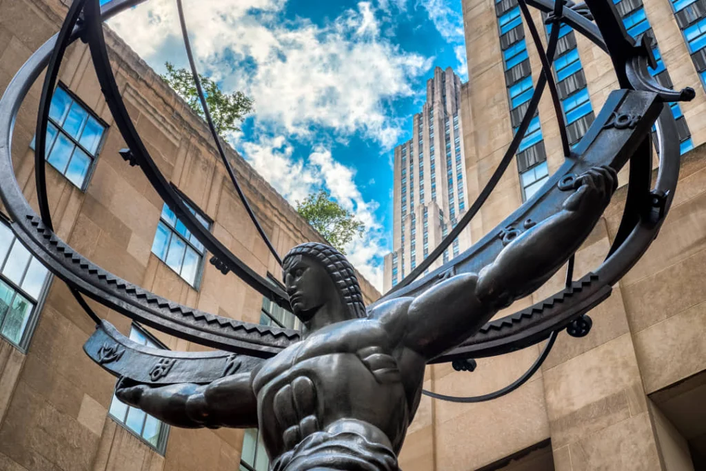 Gespierd bronzen standbeeld van Atlas die een hemelbol draagt, gefotografeerd van onderaf met wolkenkrabbers van het Rockefeller Center erachter