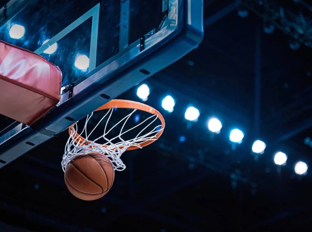 Close-up van een basketbal die door de basket en het net valt met felle lampen op de achtergrond