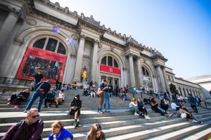 Tientallen bezoekers zitten en staan op de brede stenen trap voor de ingang van het Metropolitan Museum of Art in New York