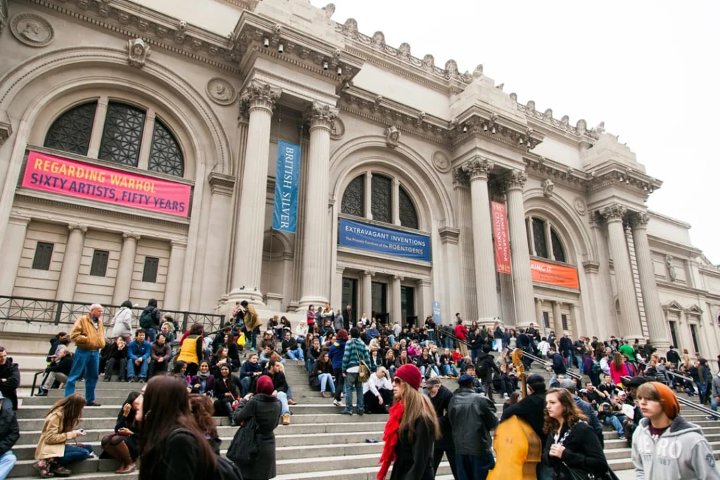 Grote groep bezoekers zit en staat op de brede trappen voor de ingang van het Metropolitan Museum of Art in New York